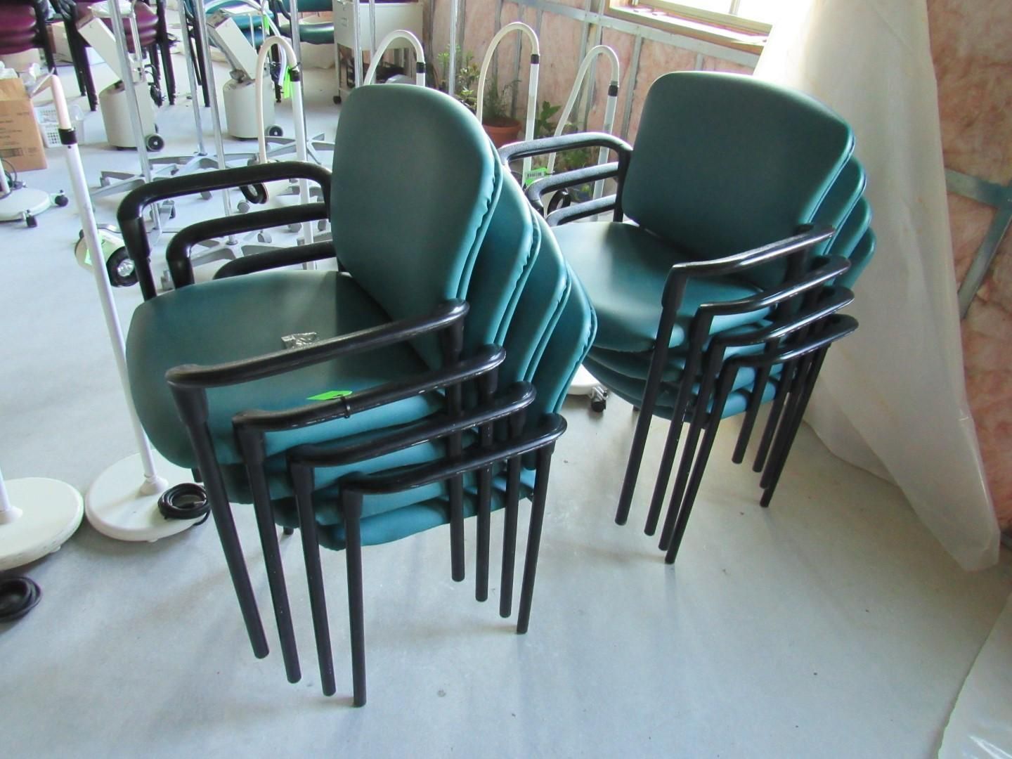 Stacks of teal armchairs with black metal frames in a room.