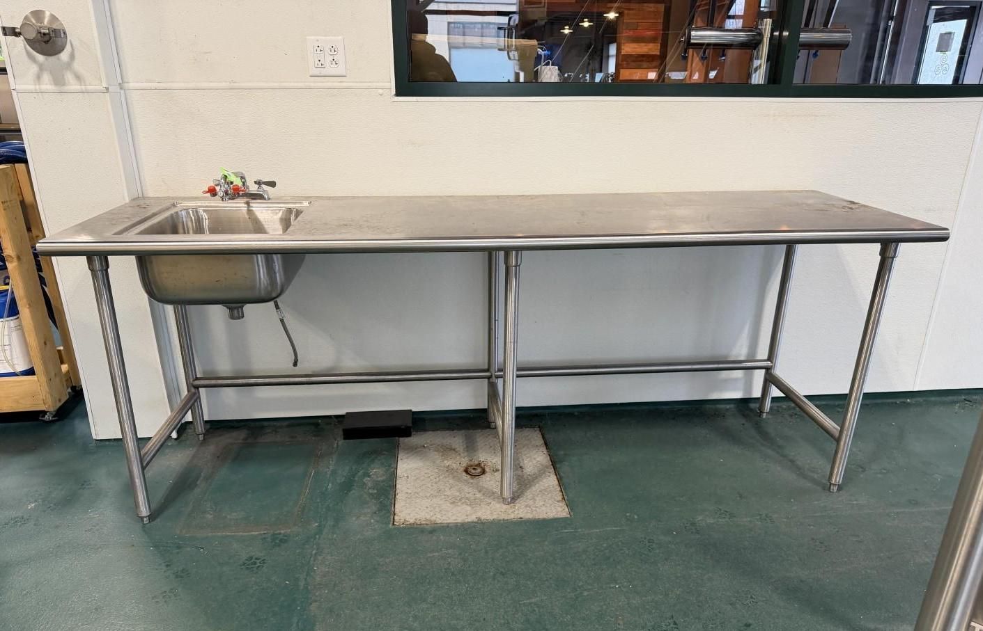 Stainless steel commercial sink on legs in a food prep area with a window in the background.
