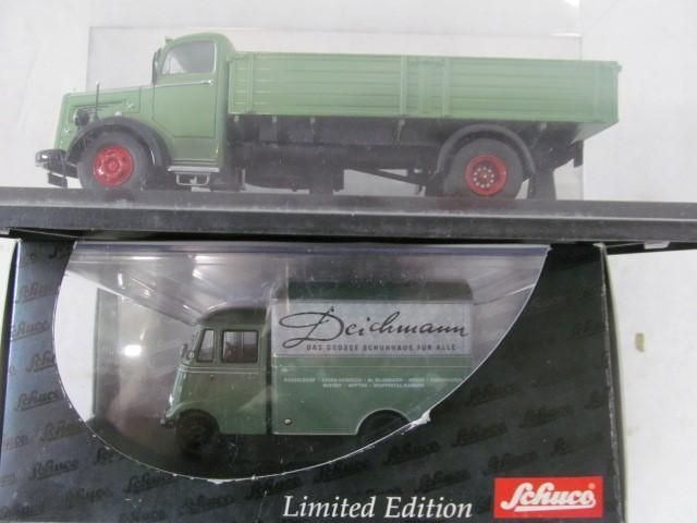 Two green model trucks in display boxes; one with a flatbed, the other a delivery van with