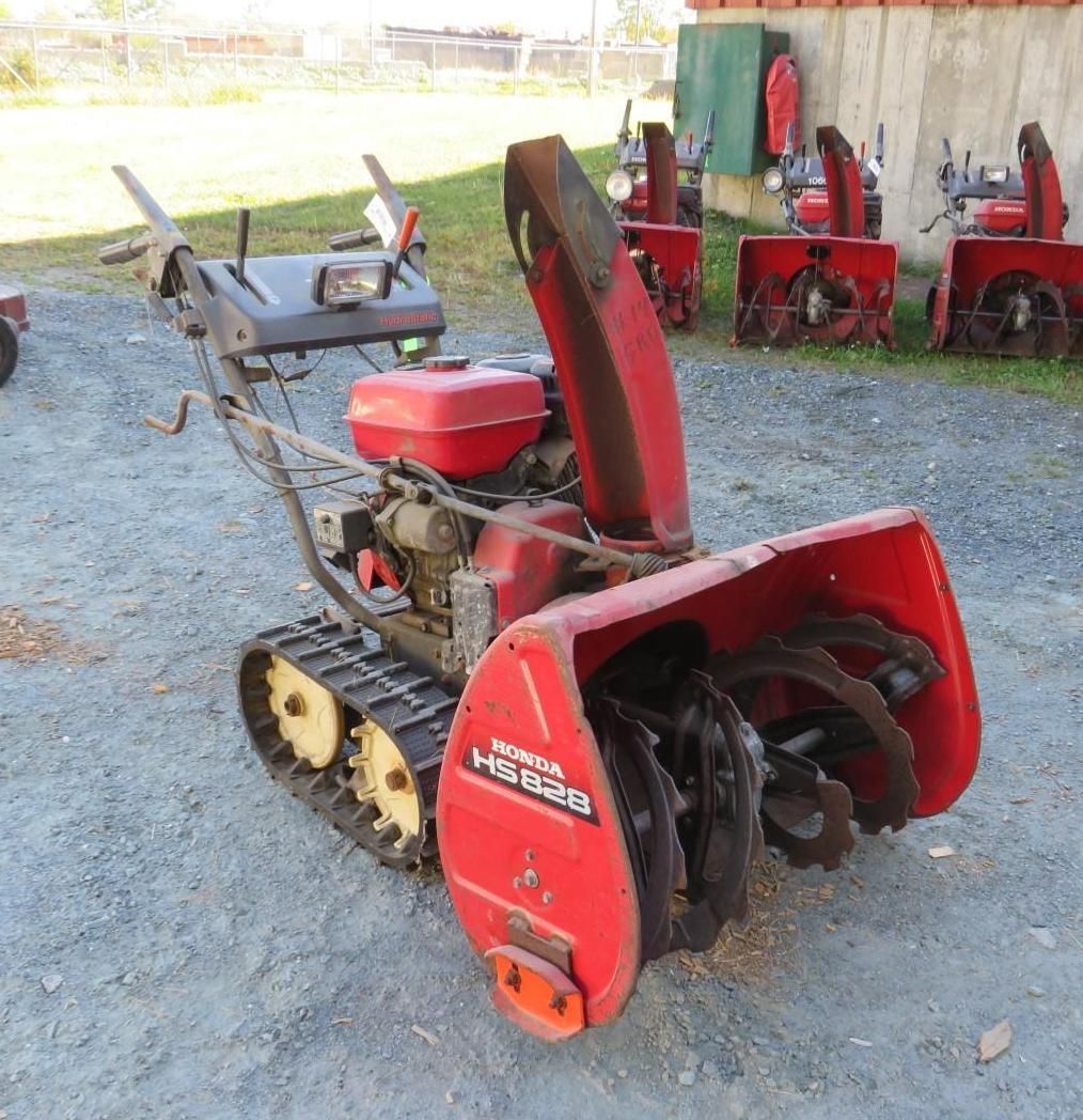 Red Honda snowblower with tracks, angled slightly to the left, on a concrete surface.