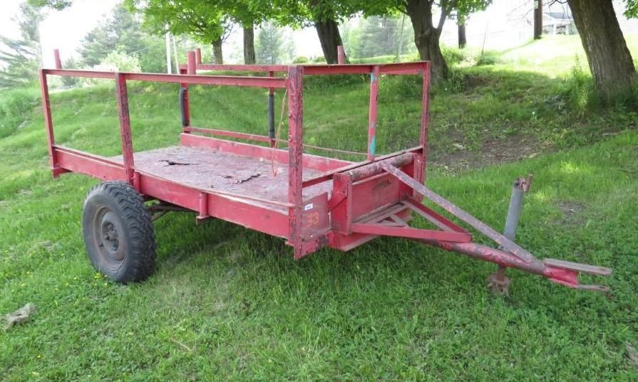 Red utility trailer on grass with cage sides, parked outdoors.