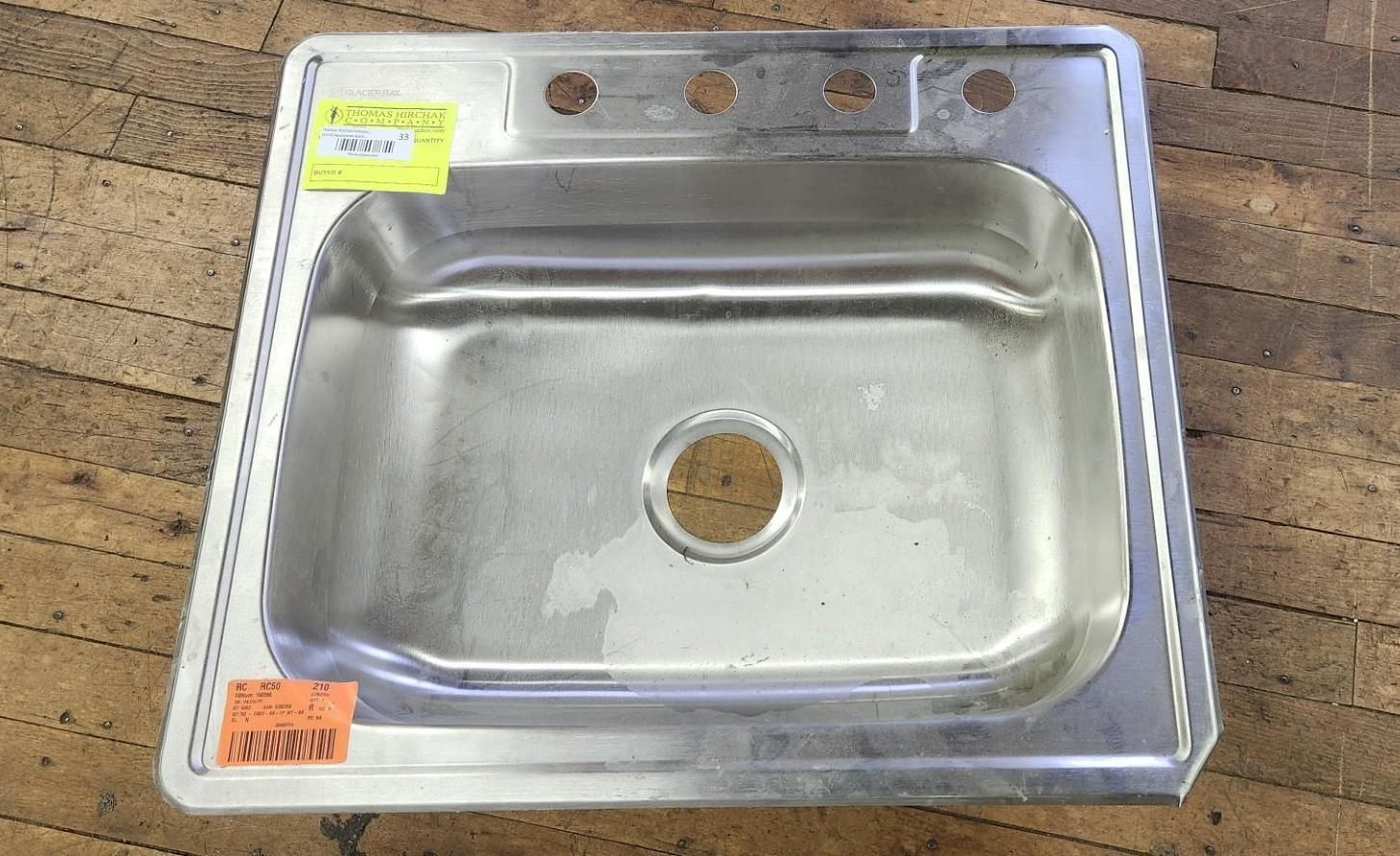 Stainless steel kitchen sink with faucet holes and price tags, on a wooden surface.