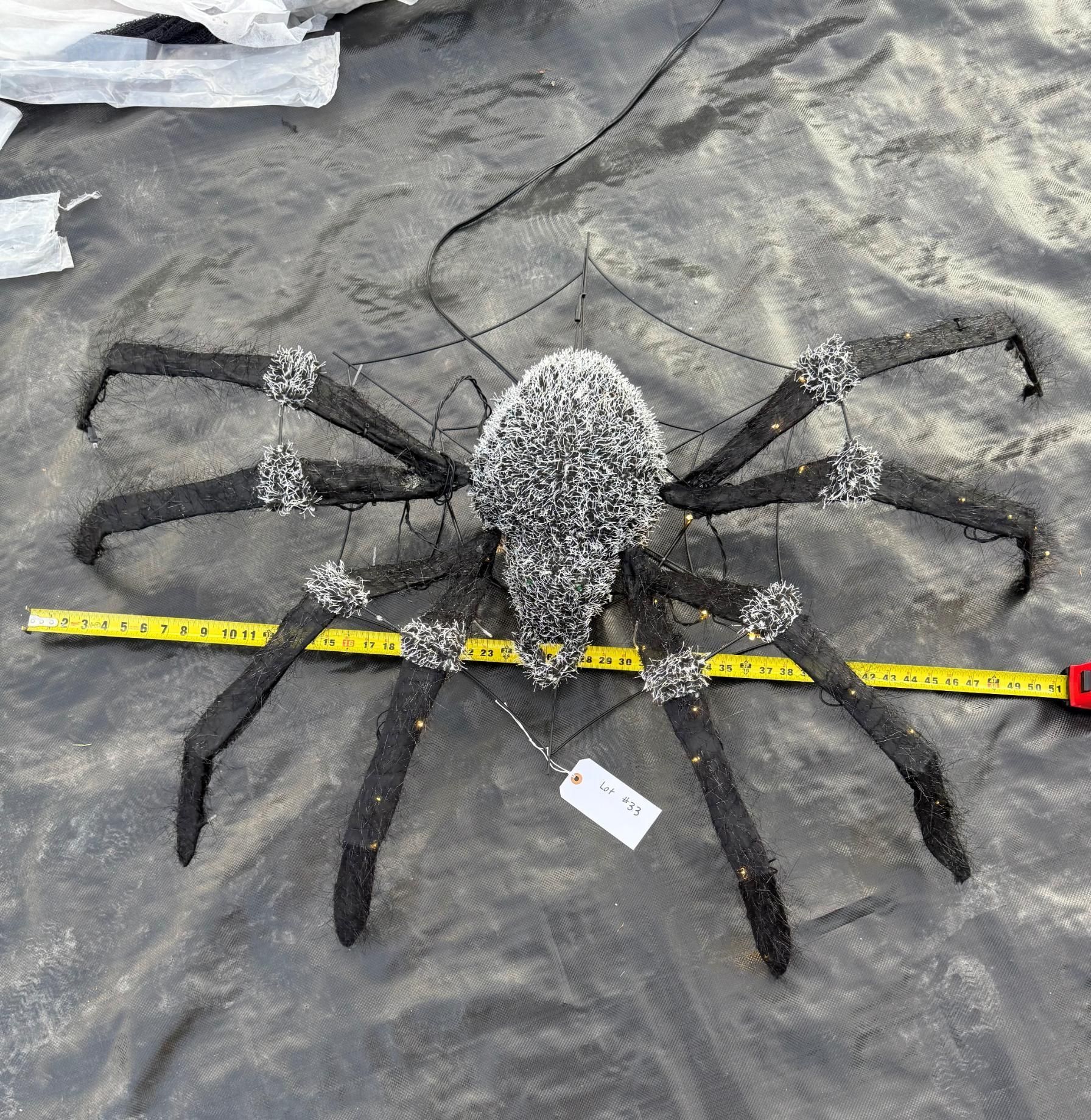 A large black spider decoration with glitter, on a black tarp. A measuring tape lies across its body. Halloween Decoration.