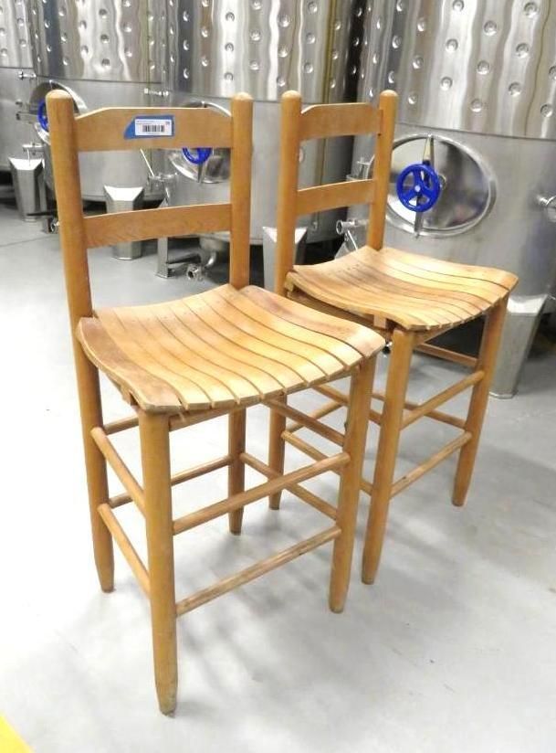 Two wooden bar stools with slatted seats in front of steel tanks.