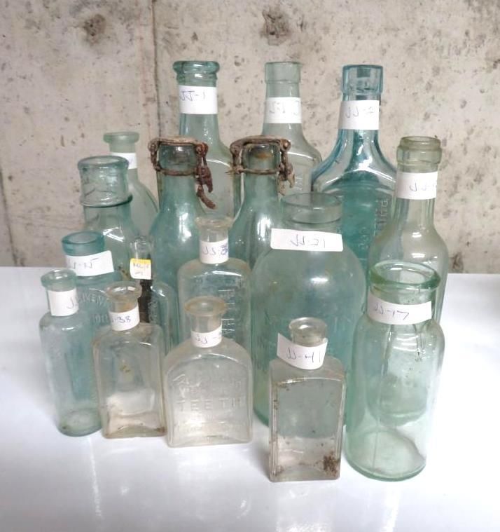 Collection of assorted antique glass bottles with labels, in varying shapes and sizes.