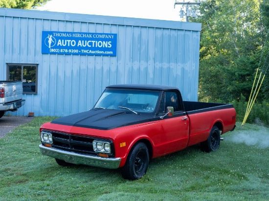 Red and black classic pickup truck parked in front of a blue building with an auto auction sign.