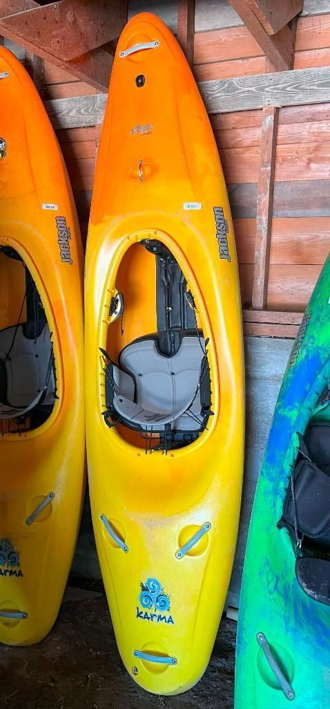 Three colorful kayaks leaning against a wooden wall. The central kayak is yellow with an orange top.