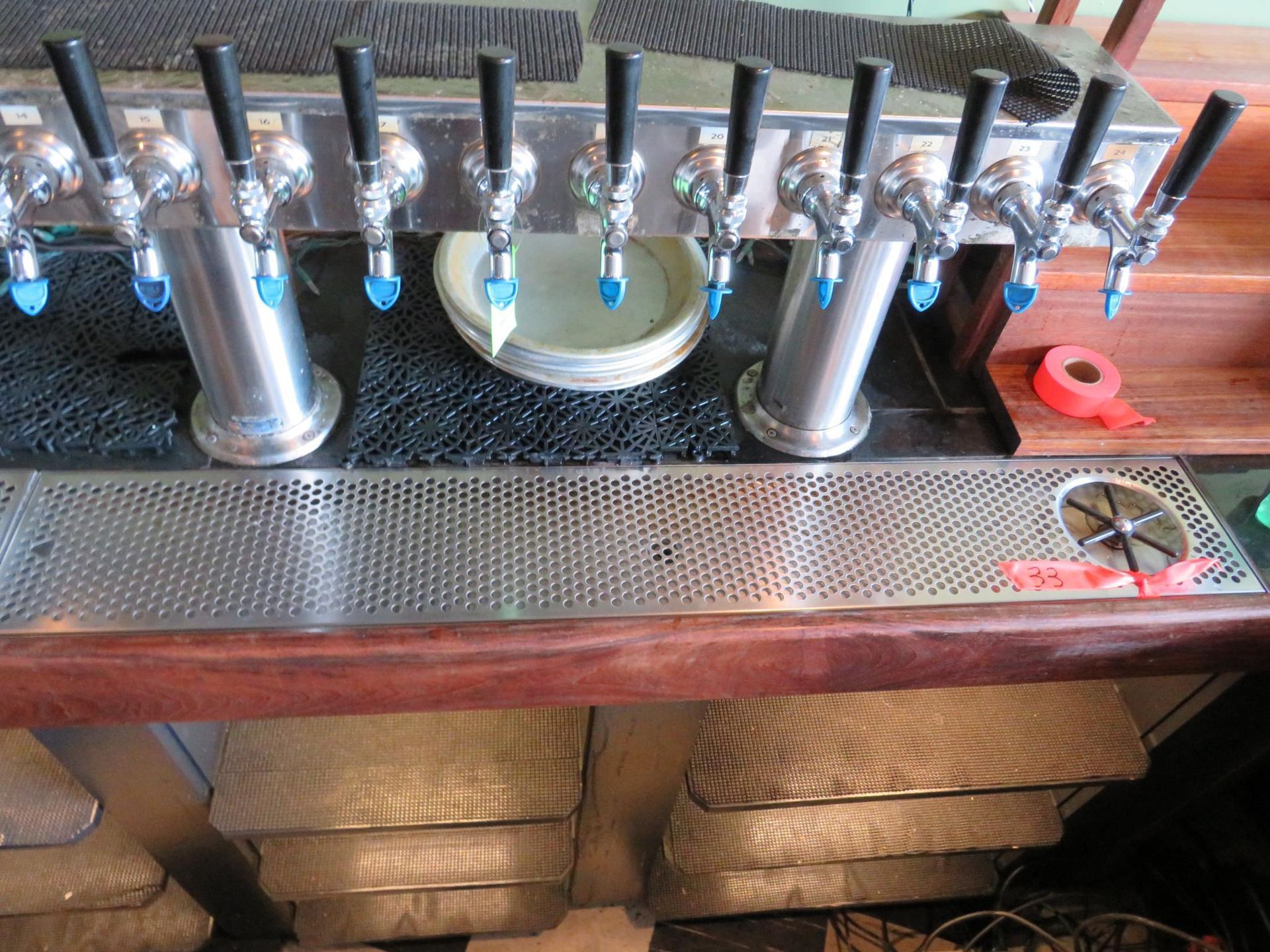 Beer taps at a bar with silver handles, blue accents, and a perforated stainless steel drip tray.
