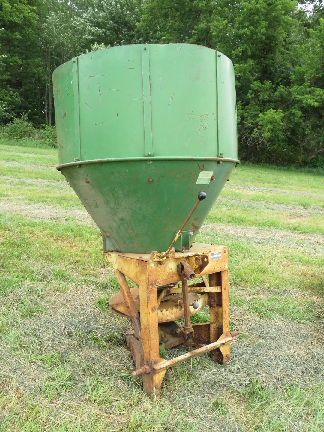 Green and yellow agricultural fertilizer spreader in a grassy field.