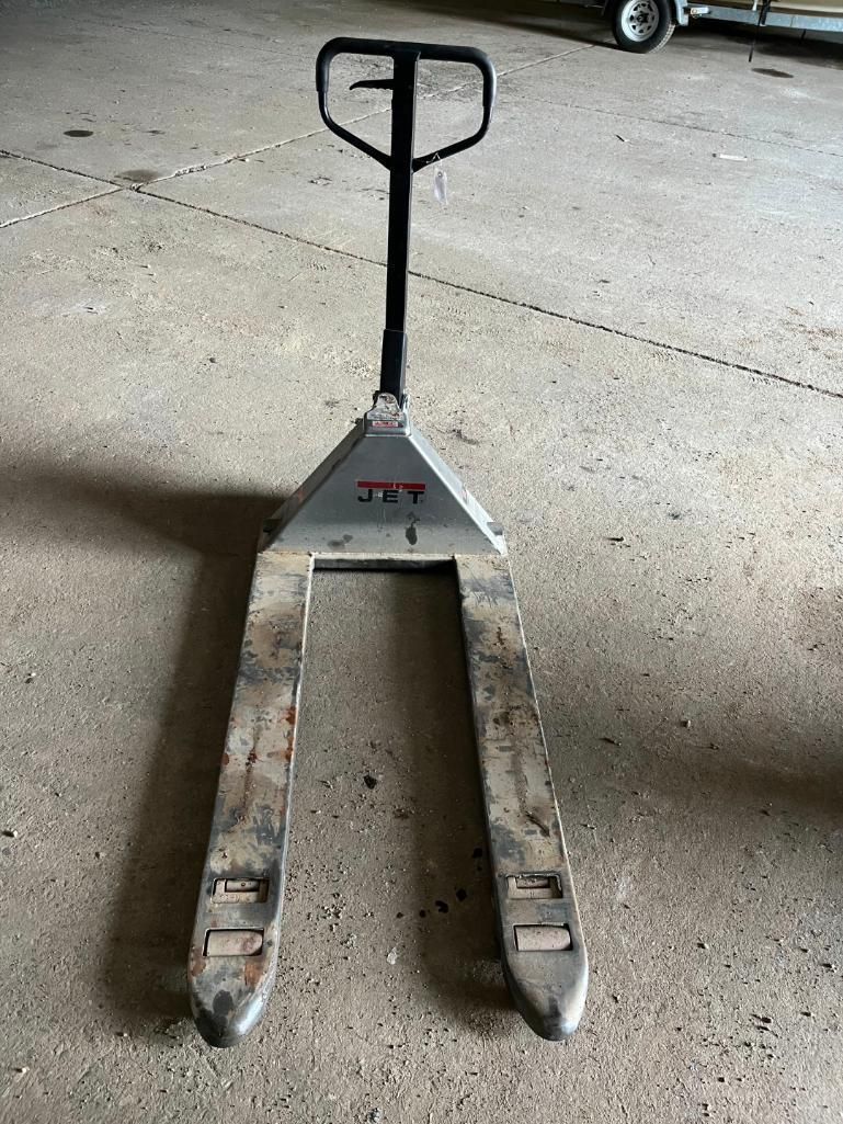 Pallet jack on concrete floor. It has a black handle and silver forks.