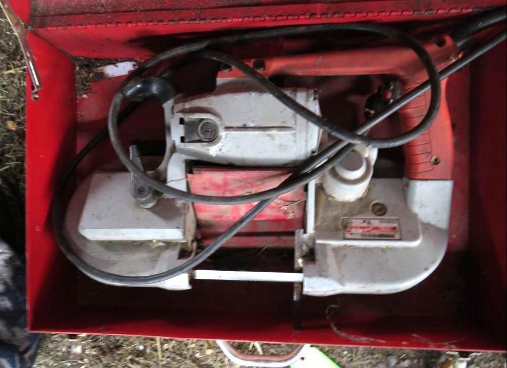A metal-cutting band saw machine in a red tool case, with a black power cord coiled inside.