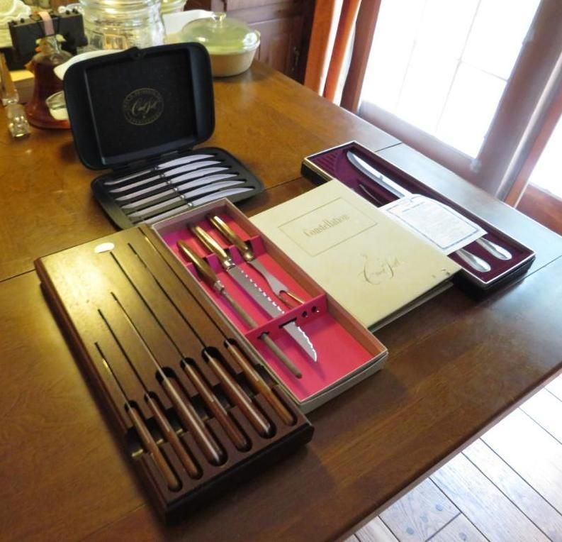 Various vintage cutlery sets in open boxes on a wooden table.
