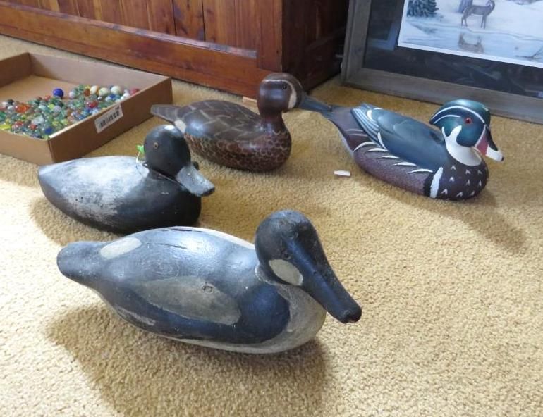 Four carved wooden duck decoys on a beige carpet, with a box of marbles and a framed photo in the background.