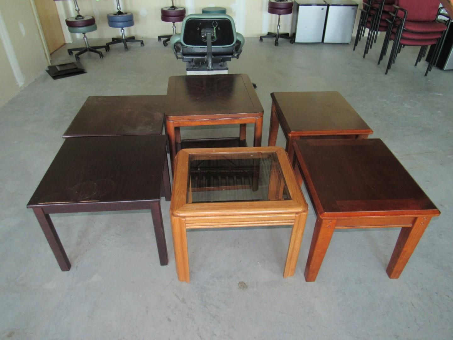 Seven wooden square tables of varying shades and a glass top table.