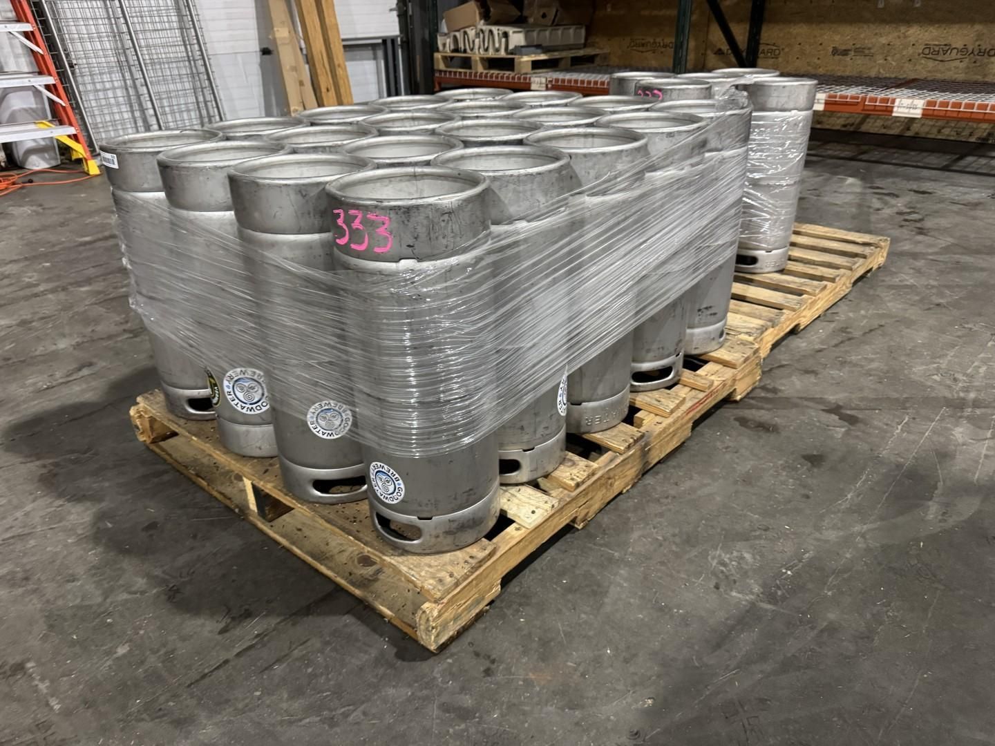 A pallet of silver beer kegs wrapped in plastic in a warehouse setting.