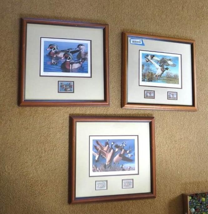 Three framed duck prints with stamps on a textured wall.