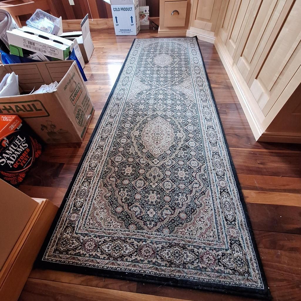 Long, patterned rug on hardwood floor, flanked by boxes and cabinets.