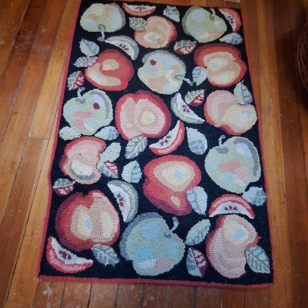 Apple-themed hooked rug on a wooden floor; apples in various colors with green leaves on a black background.