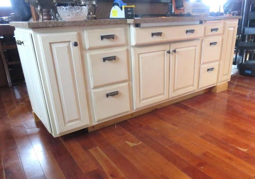 Cream-colored kitchen cabinets with black hardware and a granite countertop sit on a wood floor.