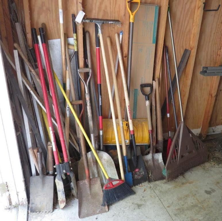 Tools leaning against a wooden wall; shovels, rakes, brooms and other gardening tools.