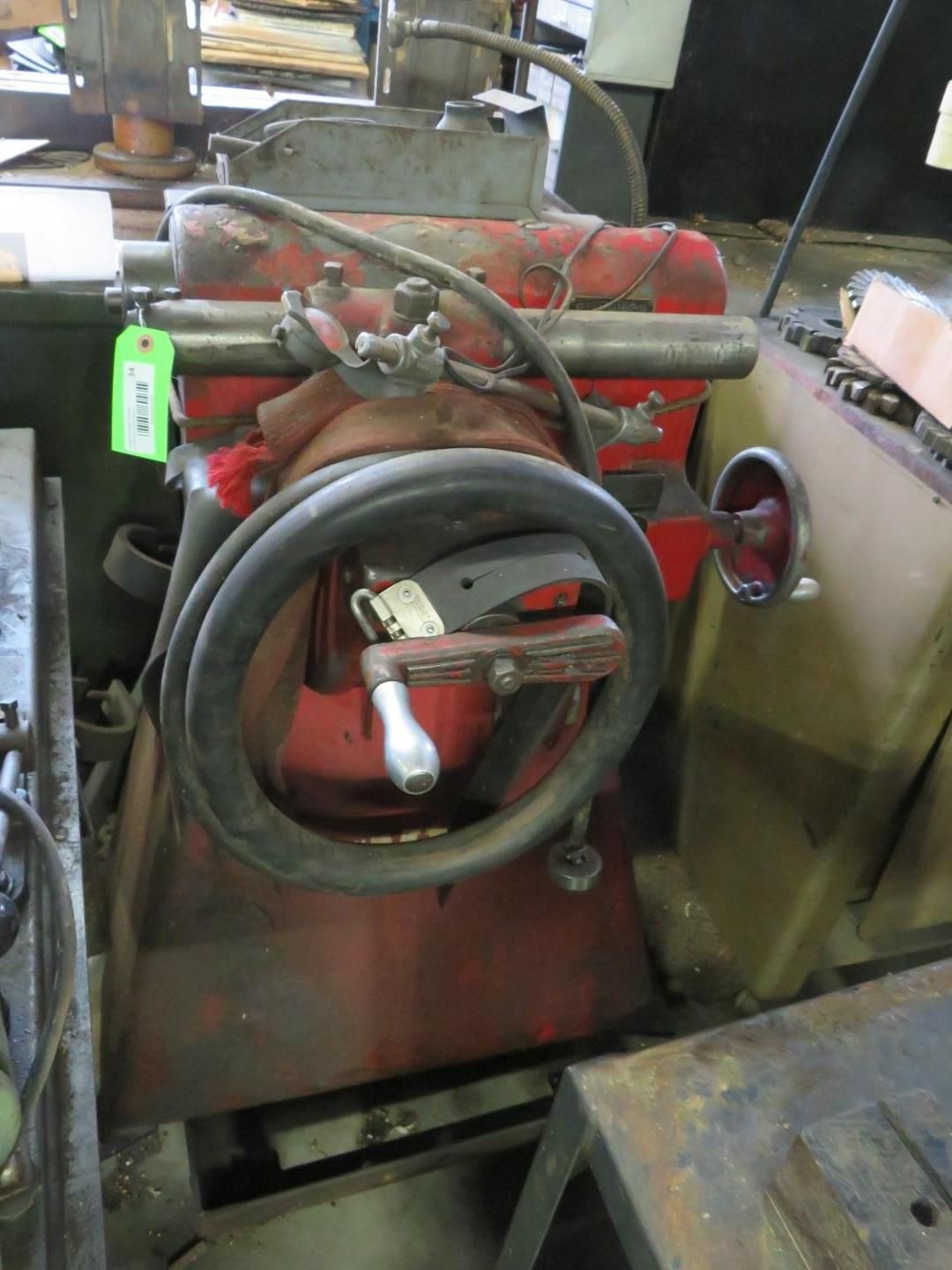 Red and gray industrial machine with a large circular handwheel and various levers.