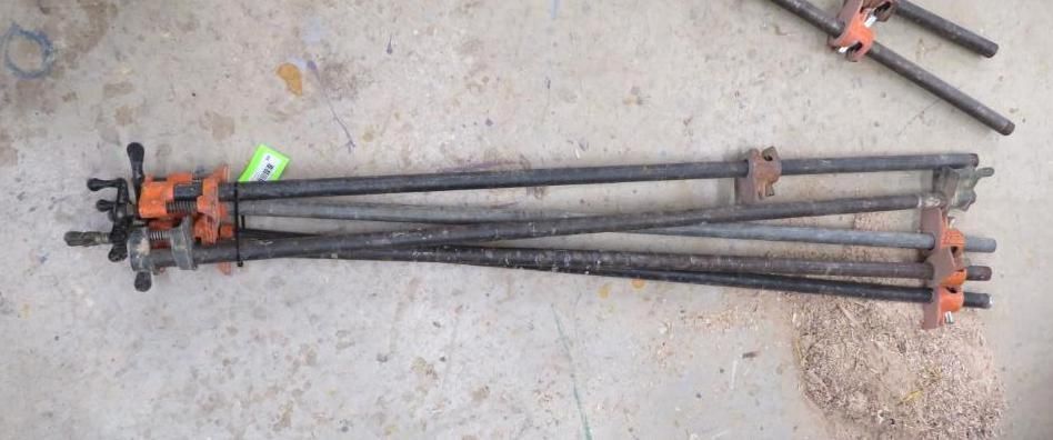 Clamps on the ground. Several long metal bars, orange clamps, and a green tag.