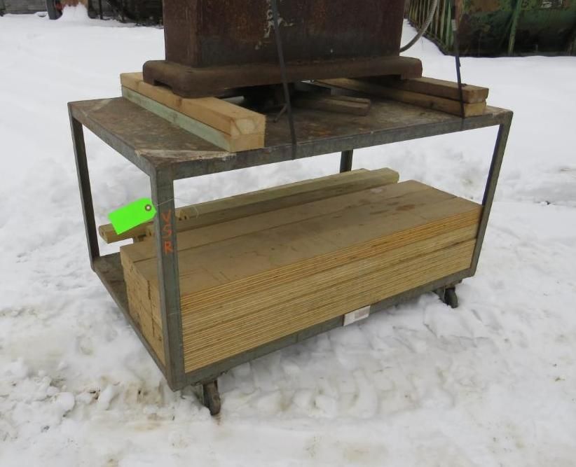 Metal cart with two shelves. Top shelf holds a heavy object and wood blocks. Bottom shelf has stacked wood. Outdoors, snow.