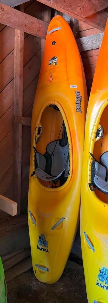 A yellow and orange kayak with a gray seat is propped in a wooden shed next to another kayak.