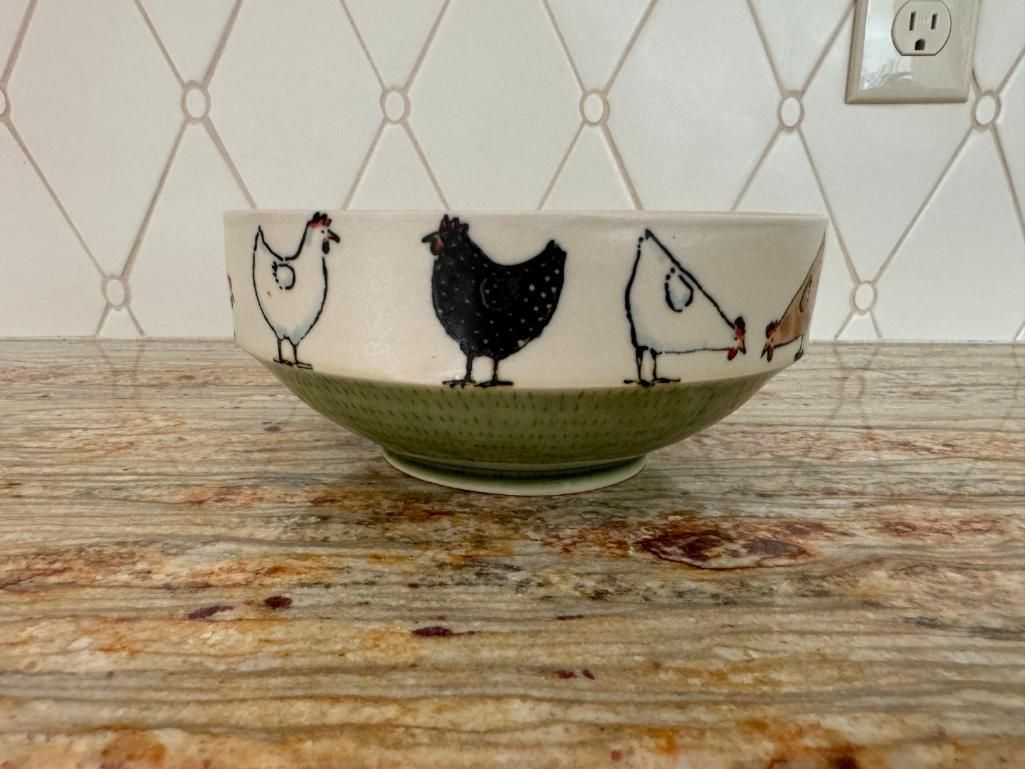 Ceramic bowl with chickens drawn around the rim, green base, on a speckled countertop.