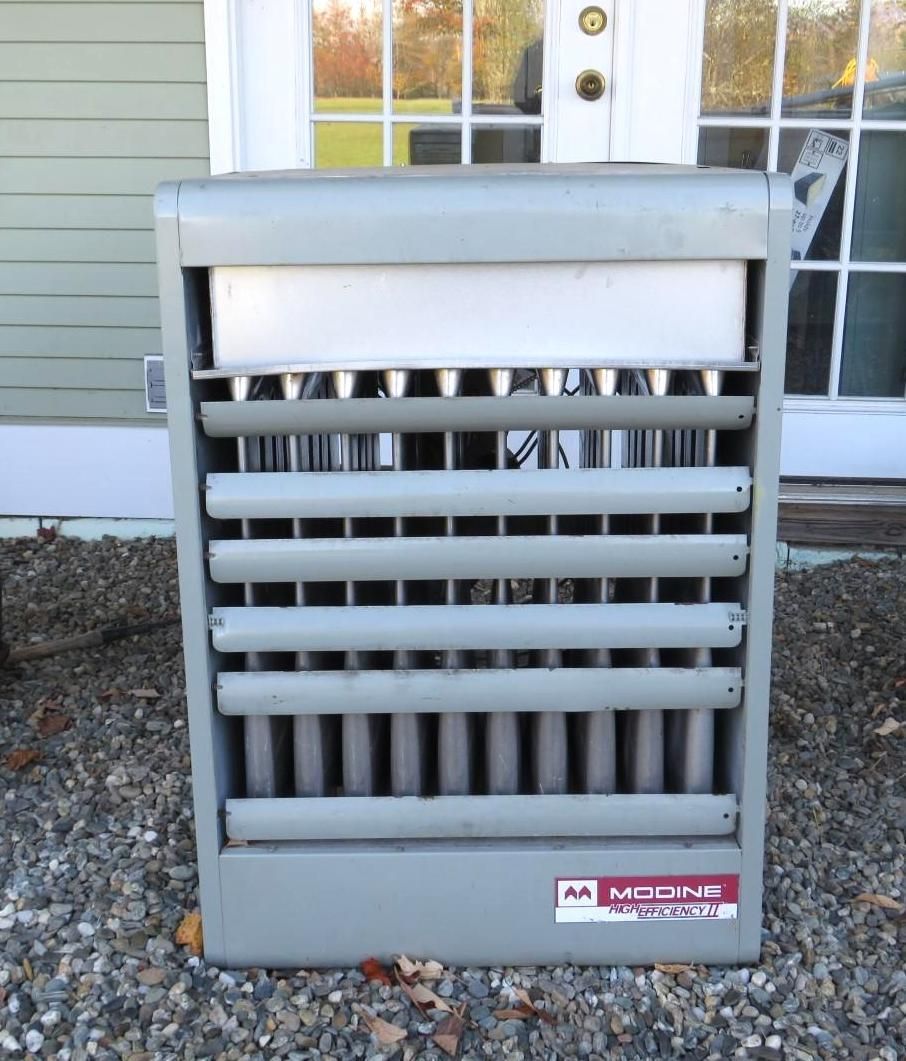 Gray industrial-style heater outside a building with glass doors, resting on gravel.