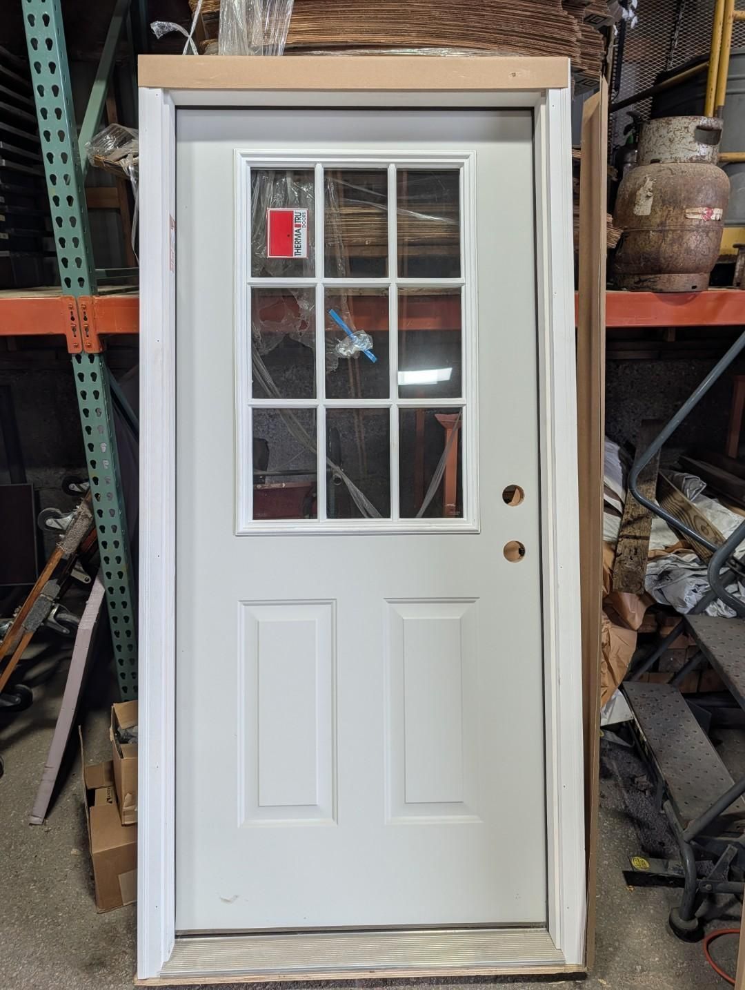 White exterior door with a window, leaning in a storage area with shelves and tools around it