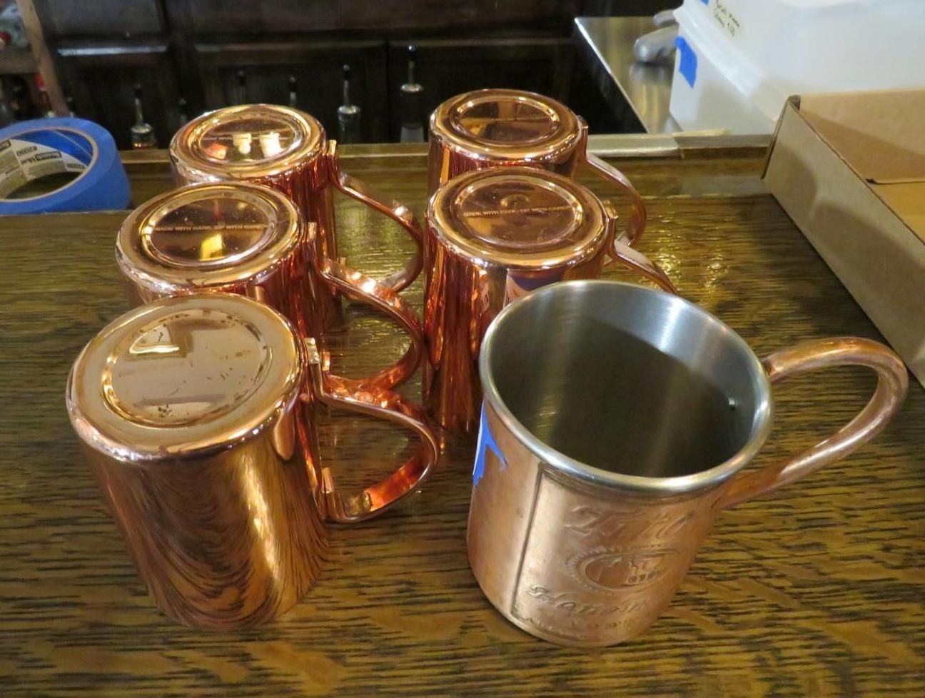 Copper mugs, some upright, others in a holder, sit on a bar. One is empty.