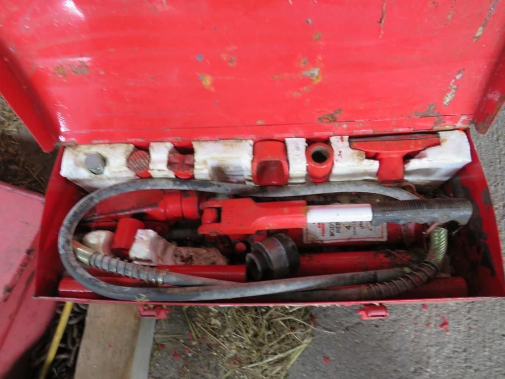 Red toolbox open, containing a hydraulic jack and assorted attachments.