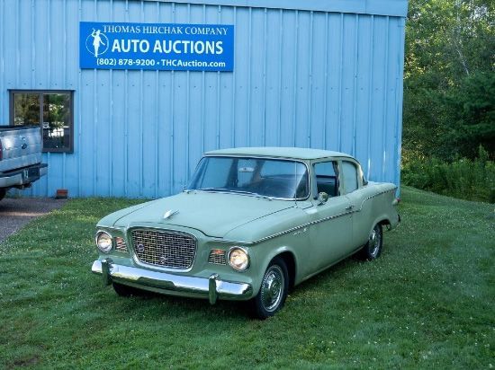 Green vintage Studebaker car parked in front of a blue Thomas Hirchak Company Auto Auctions building.