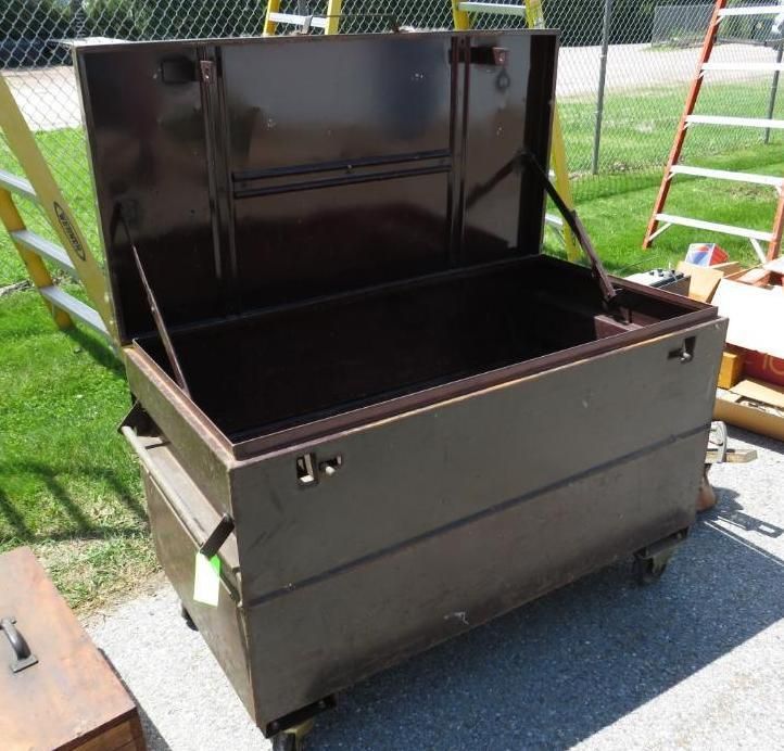 Brown metal toolbox with open lid, set on wheels, outdoors.