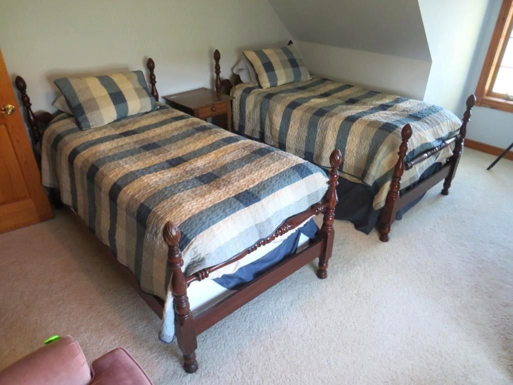 Two twin beds with plaid bedding in a room with a slanted ceiling and a window.