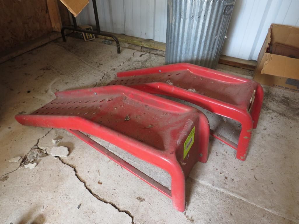 Two red plastic car ramps on a concrete floor in a garage.