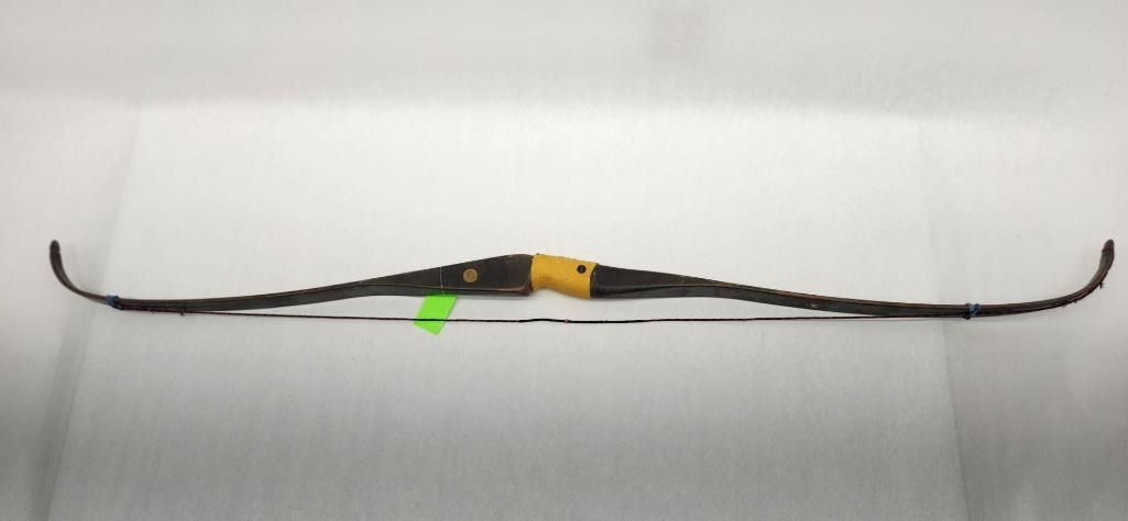 Black recurve bow on a white surface, viewed from above. Green sticker near the center.