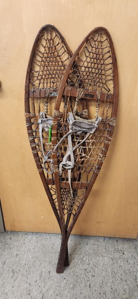 Pair of vintage wooden snowshoes. Brown, heart-shaped frames with a woven interior and attached foot straps.