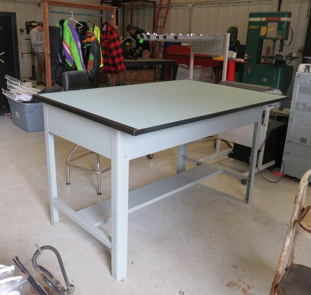 A light gray drafting table with a dark border, in a workshop setting.