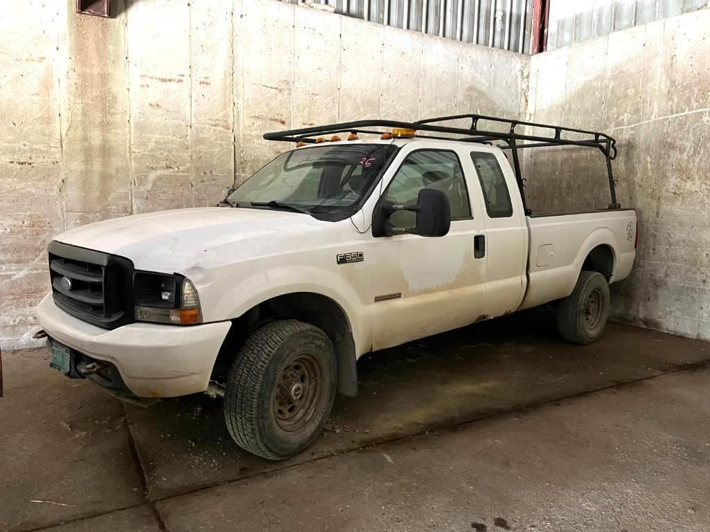 White pickup truck with a rack and bed topper parked against a concrete wall.