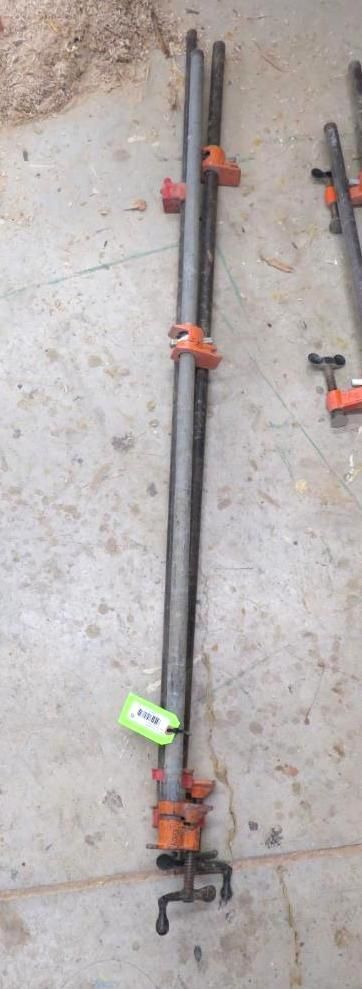 Two long, black pipe clamps with orange ends, resting on a gray concrete surface.