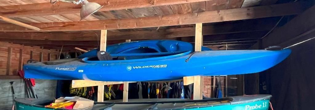 Blue kayak suspended from a wooden ceiling in a storage shed.