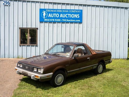 Brown Subaru Brat pickup truck parked in front of a blue sign with 
