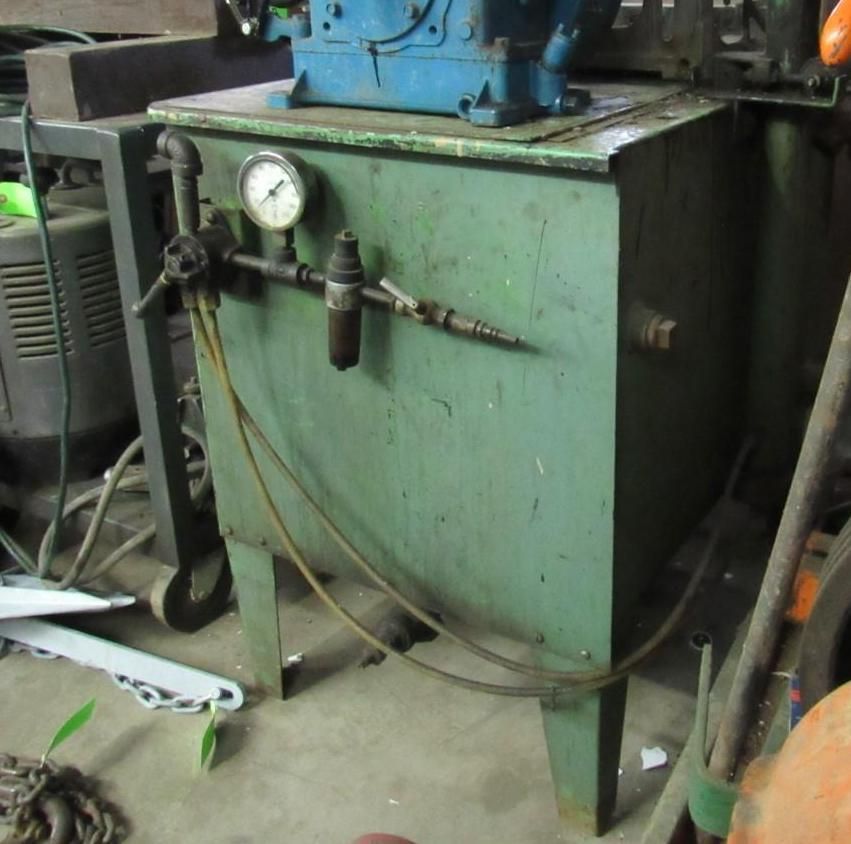 Green metal tank with gauge, piping, and blue machinery on top, set in a workshop.