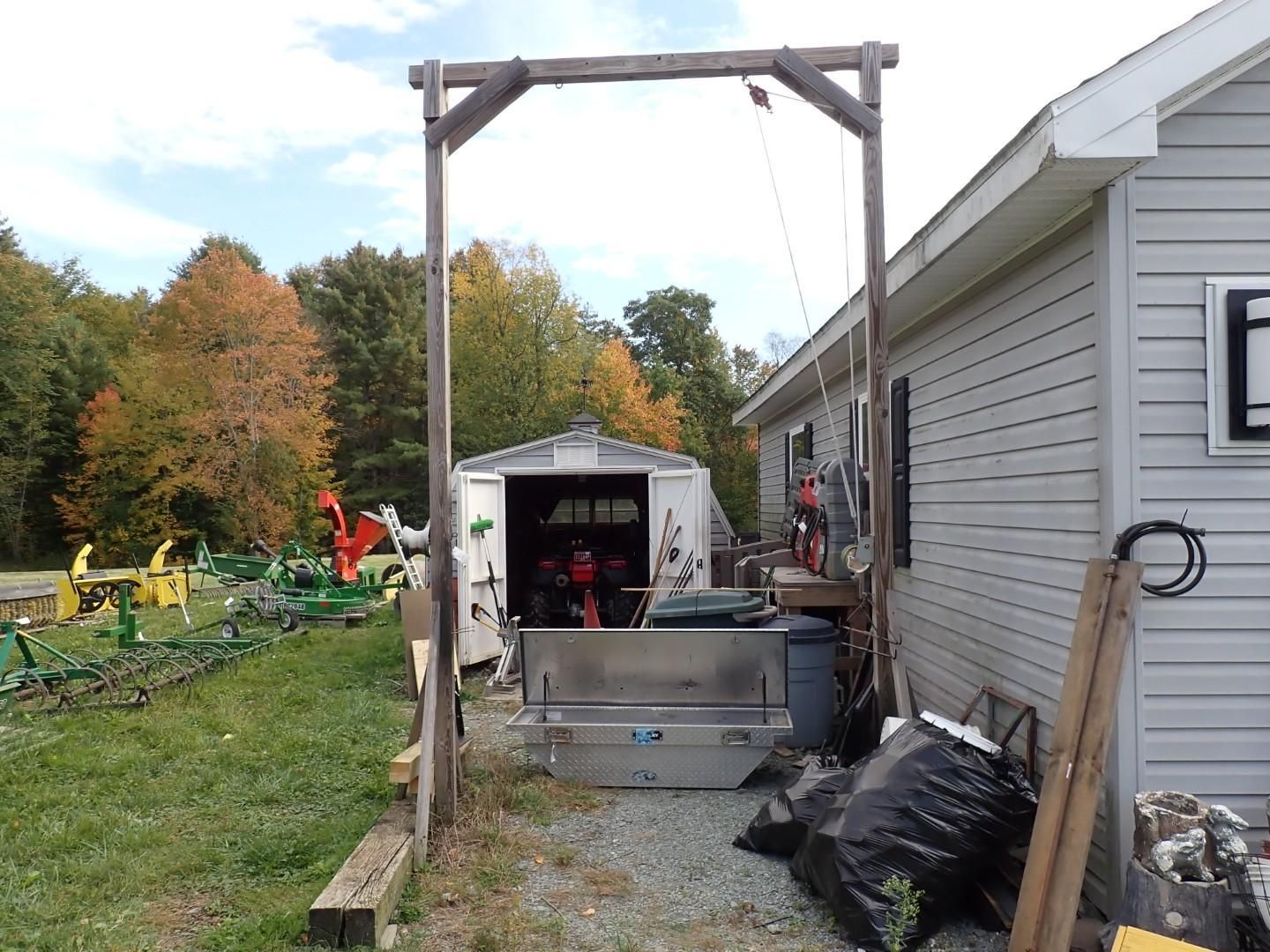 Backyard work area with shed, wooden frame, tools, and large metal tub beside a house