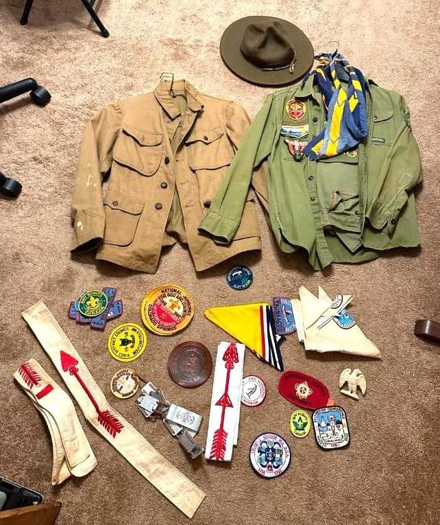Scout uniform jackets, hat, neckerchief, and patches on a carpet.