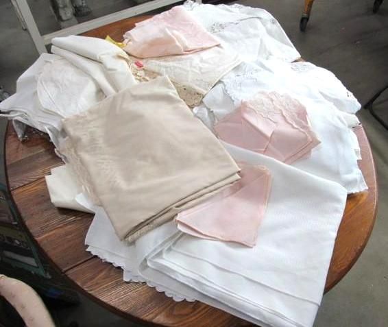 Pile of folded linens, including white, cream, and pink sheets and napkins on a wooden table.