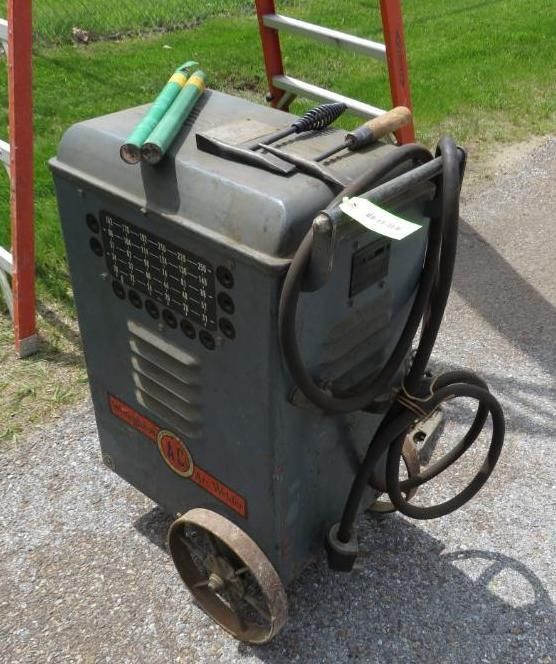 Gray welding machine on wheels with tools and green rods, outdoors.