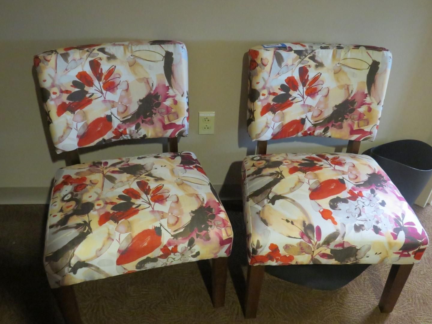 Two chairs with floral upholstery, brown wood frames, set against a beige wall.